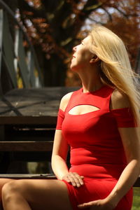 Woman with blond hair looking up while sitting by bridge on sunny day