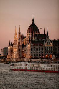 Hungarian parliament building by river against clear sky at sunset