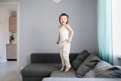 Cute european child toddler in light clothes jumps on gray sofa in living room