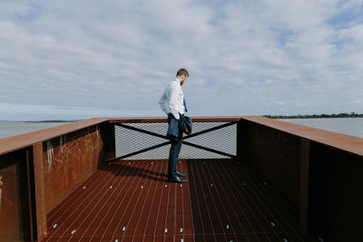 Side view of man standing by sea against cloudy sky