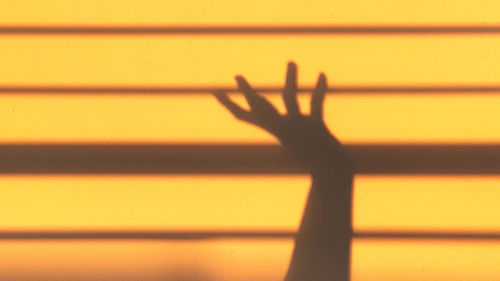 Shadow of person hand on yellow wall