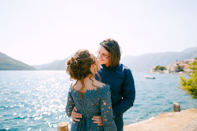 Friends standing against sea and mountains against sky