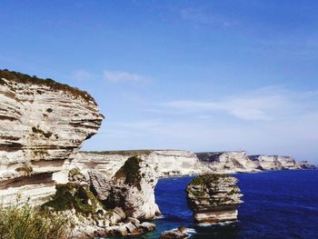 Rock formations by sea against blue sky