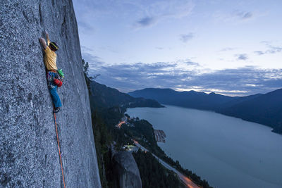 Side view man rock climbing at sunset above the sea and highway