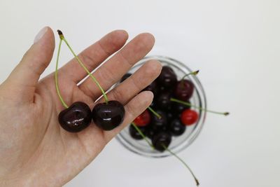 Close-up of hand holding strawberry over white background