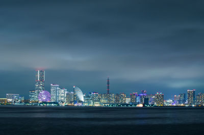 Illuminated city by sea against sky