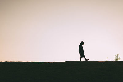 Side view of woman walking on field against clear sky