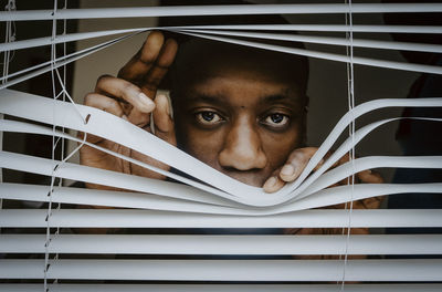 Depressed man looking out of window blinds at home