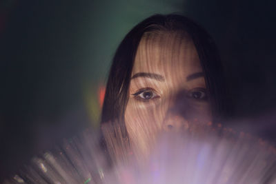 Close-up portrait of young woman holding illuminated fiber optic in darkroom