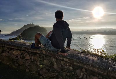 Rear view of man sitting on mountain against sky