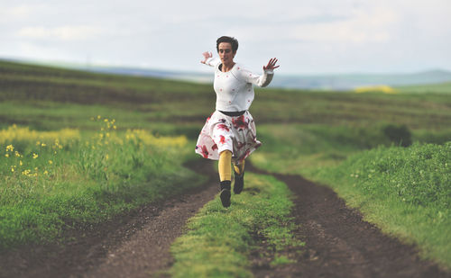 Full length of woman jumping over field against sky