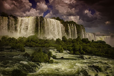 Scenic view of waterfall against cloudy sky