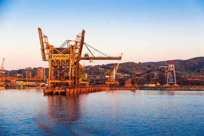 Cranes at commercial dock against clear sky