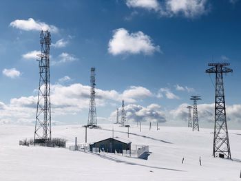 Electricity pylon on snow covered field against sky