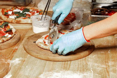 Close-up of the hands of a caucasian man wearing blue latex gloves cutting a cooked pizza on  board.