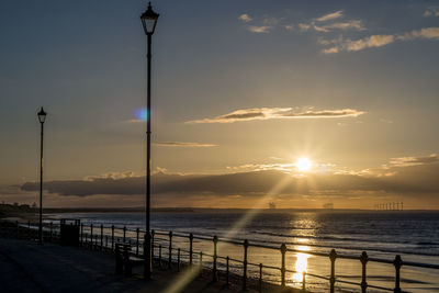 Silhouette street by sea against sky during sunset