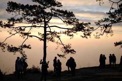 Silhouette people standing by tree against sky during sunset