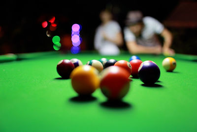 Close-up of colorful pool balls on table with friend playing in background