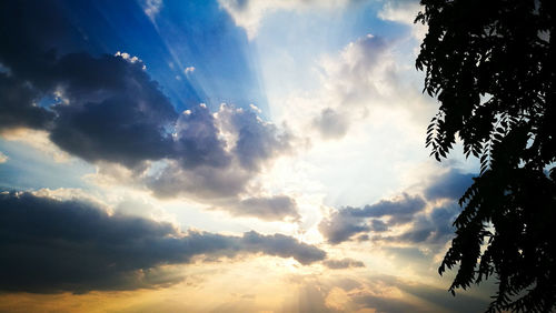 Low angle view of sunlight streaming through clouds