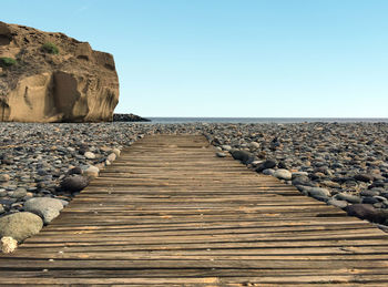 Boardwalk leading towards sea against clear sky