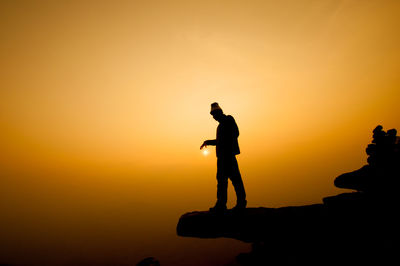 Silhouette of man standing on cliff against sky during sunset