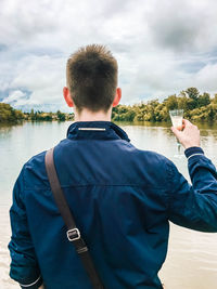 Rear view of man standing by lake against sky