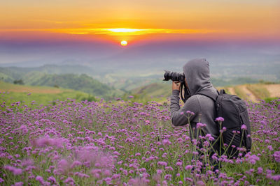 Man photographing flowering plants against sky during sunset