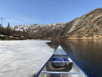 Canoe on mountain lake with ice by snowcapped mountains against blue sky