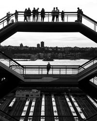 People on footbridge over river in city against sky