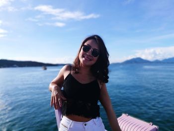 Portrait of smiling young woman standing by sea against sky