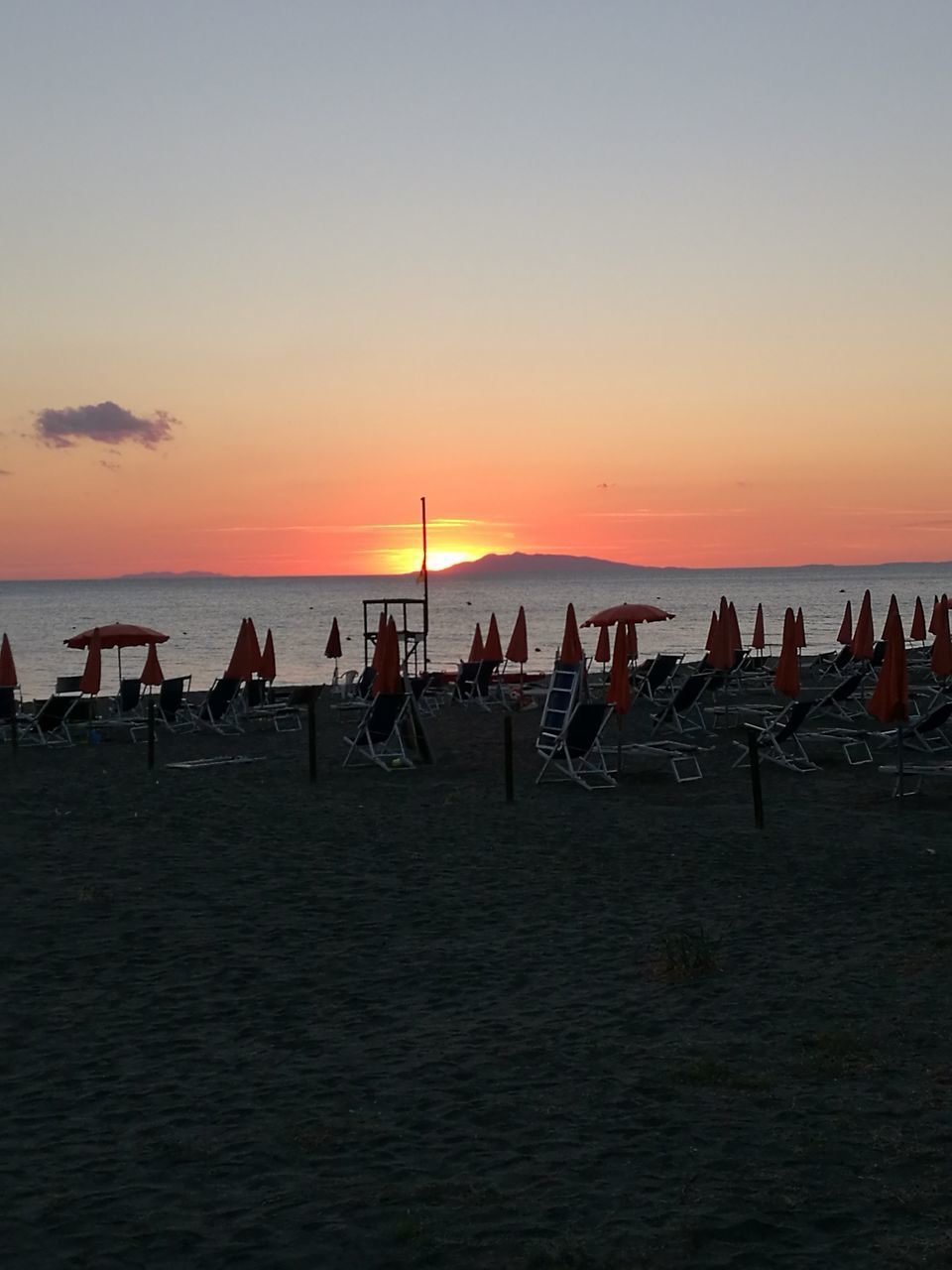 sunset, water, large group of people, sea, horizon over water, silhouette, beach, vacations, standing, tourism, tourist, sky, leisure activity, scenics, tranquility, tranquil scene, weekend activities, togetherness, orange color, nature, dramatic sky, beauty in nature, solitude, outdoors, atmospheric mood, ocean, outline, atmosphere