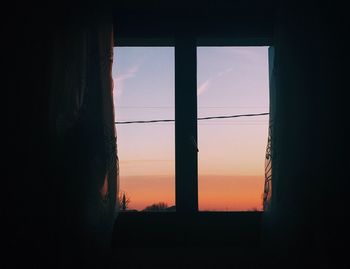 Silhouette buildings seen through window during sunset