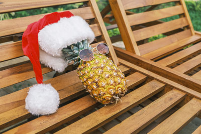 Side view of relaxing funny pineapple wearing sunglasses and santa claus hat lies on wooden sunbed 