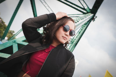 Woman wearing sunglasses against metallic structure and sky