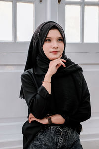 Portrait of young woman standing against wall