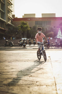 Kid riding bicycle on street in city, against the sunlight