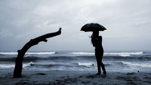 Silhouette woman holding umbrella on beach against sky