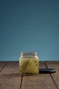 Jar with fond of gherkin pickles on wooden table with blue background