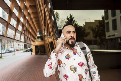 Casual wear man standing against office building while using mobile