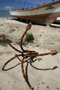 Rusty anchor by moored boat at beach against sky