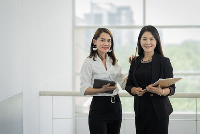 Portrait of cheerful businesswoman standing with colleague in modern office