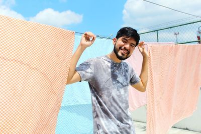 Smiling man standing by clothesline against sky