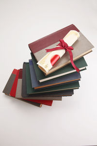 Close-up of diploma on stacked books against white background