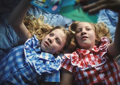 Cute sisters reading book on bed at home