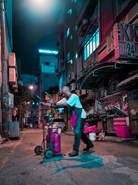 People standing on illuminated street amidst buildings in city at night