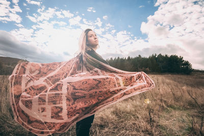 Young woman with arms raised on field against sky