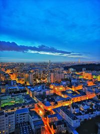 High angle view of illuminated city buildings against blue sky