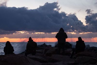 Silhouette of people on beach against cloudy sky