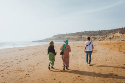 Rear view of people walking at beach against sky