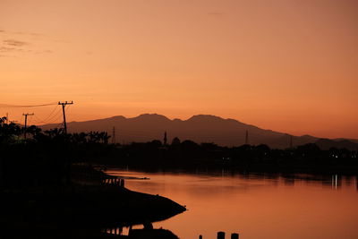 Scenic view of lake by silhouette mountains against orange sky